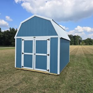 A vibrant Slate Blue Premier Lofted Barn with crisp white trim and a contrasting white metal roof, set against a lush green lawn under a bright blue, cloudy sky, showcasing its classic barn-style design and double doors.