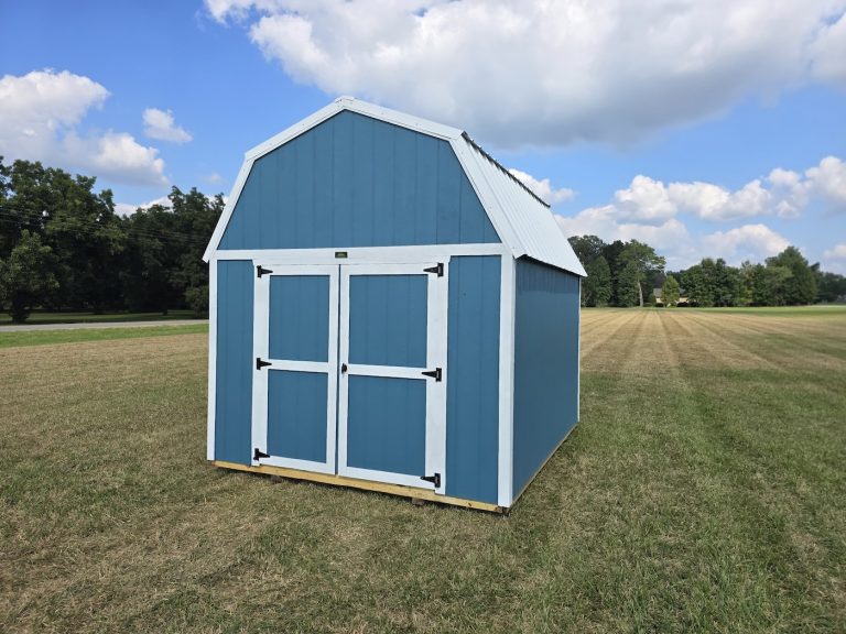 A vibrant Slate Blue Premier Lofted Barn with crisp white trim and a contrasting white metal roof, set against a lush green lawn under a bright blue, cloudy sky, showcasing its classic barn-style design and double doors.