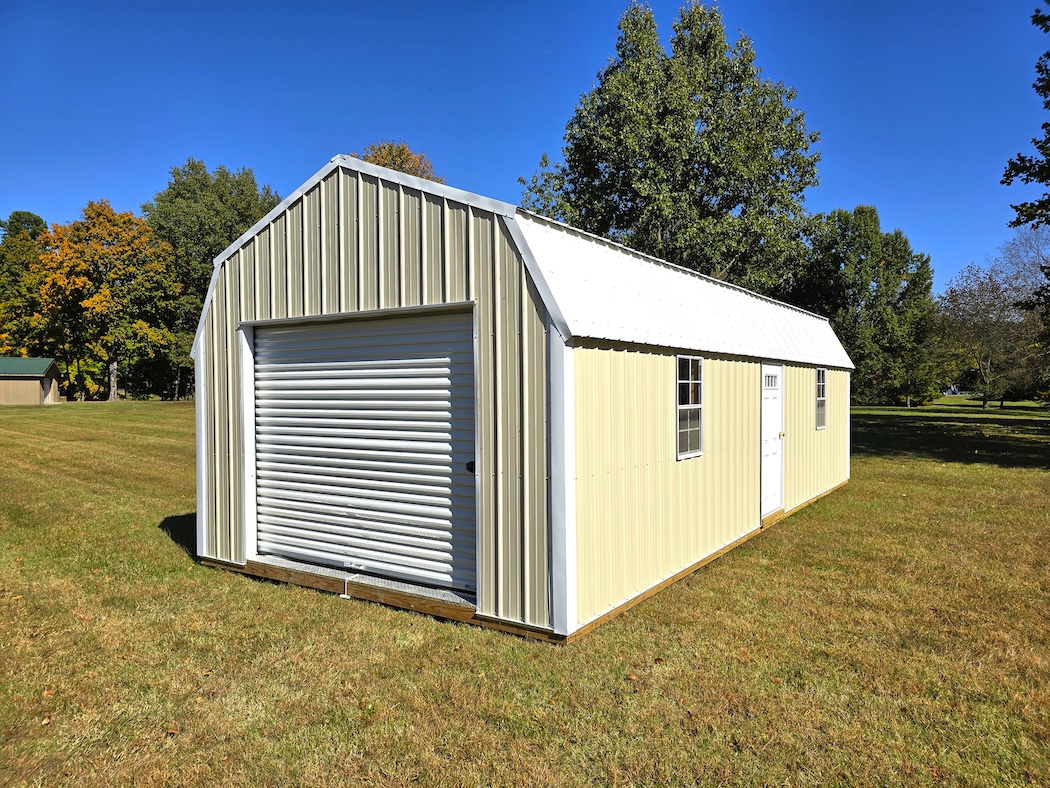 A spacious Premier Lofted Garage featuring Sandstone Metal siding, a bright White Metal Roof, a large roll-up garage door, a side entry door, and windows, set on a green lawn under a clear sky.