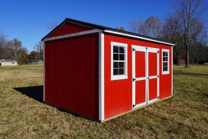 A scarlet red Premier Side Utility shed with white trim and a black roof, in a grassy field under a clear blue sky.