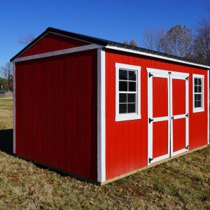 A scarlet red Premier Side Utility shed with white trim and a black roof, in a grassy field under a clear blue sky.