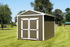 A newly installed Premier Utility shed featuring Driftwood siding and a Light Stone roof, with open double wooden doors revealing its spacious interior, set on a vibrant green lawn under a clear blue sky.