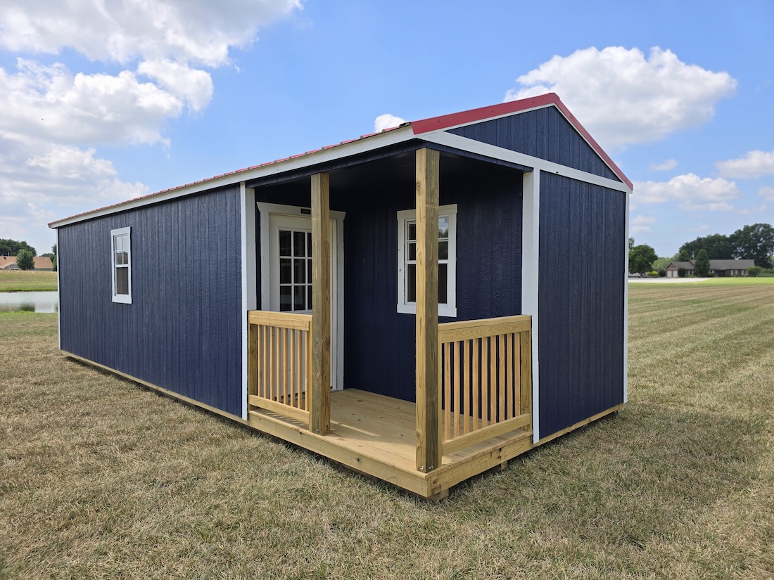 A Navy blue Premier Side Cabin with a Rustic Red roof and a small wooden porch, set in a grassy field under a partly cloudy sky.